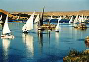 Bílé trojúhelníky štíhlých plachetnic plujících po tmavomodrém Nilu